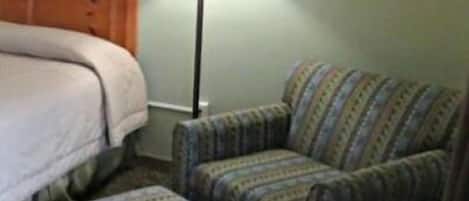 A bedroom with a bed, a nightstand, a lamp, and a patterned armchair.