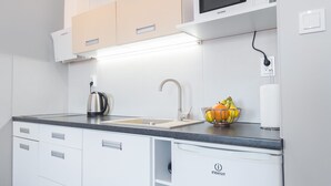 A modern kitchen with white cabinetry, a stainless steel kettle, a sink, and a fruit bowl. - Apartment Centrum (Szczecin)