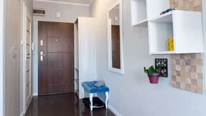A hallway with a wooden door, a white bench, a potted plant, and a wall-mounted shelf with a decorative item. - Apartment Centrum (Szczecin)