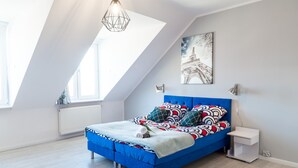 A modern bedroom with a sloped ceiling, a blue bed, patterned pillows, a radiator, and a painting of the Eiffel Tower. - Apartment Centrum (Szczecin)