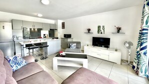Un salon moderne avec un canapé, une table basse et un téléviseur. Il y a également un coin cuisine équipé d’un réfrigérateur, d’un four à micro-ondes et d’une cuisinière.