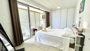 Une chambre d’hôtel comprenant un lit, un bureau avec une lampe, une chaise et une porte-fenêtre coulissante donnant sur un balcon.