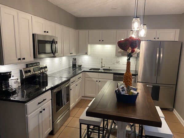 A modern kitchen with white cabinets, stainless steel appliances, and a wooden dining table.