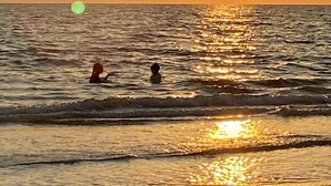 Auringonlasku tyynen meren yllä, ja vedessä on kaksi ihmistä.