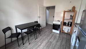 A compact kitchen with a dining table and chairs, a built-in oven, a wooden shelf with kitchen items, and a refrigerator. - New flat for 9 ★Special price per month ★ 4 Rooms (Zeitz)