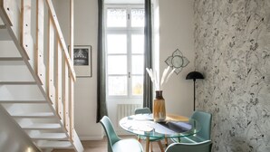 A dining area with a glass table, green chairs, a vase with white flowers, a black floor lamp, and a staircase.