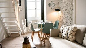 A modern living room with a staircase, a dining area with a table and chairs, and a sofa with a fluffy throw.