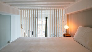 A bedroom with a bed, a bedside lamp, and a window with vertical blinds.