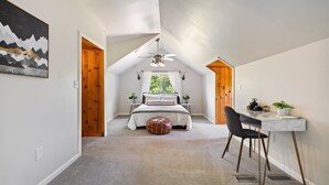 Une chambre à coucher avec un lit, un bureau et une chaise. Il y a une fenêtre avec des rideaux et un ventilateur de plafond.