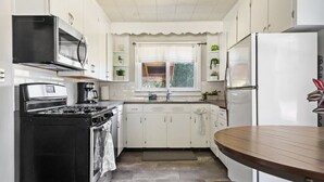 Une cuisine de taille réduite avec des meubles blancs, une cuisinière noire, un four à micro-ondes et un réfrigérateur.