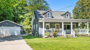 Une maison à deux étages avec un porche à l’avant, un garage et une pelouse bien entretenue.
