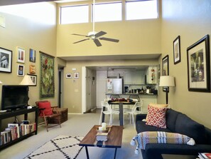 Un salon spacieux doté d’un ventilateur de plafond, d’un téléviseur, d’une bibliothèque et d’un coin repas avec une table et des chaises.