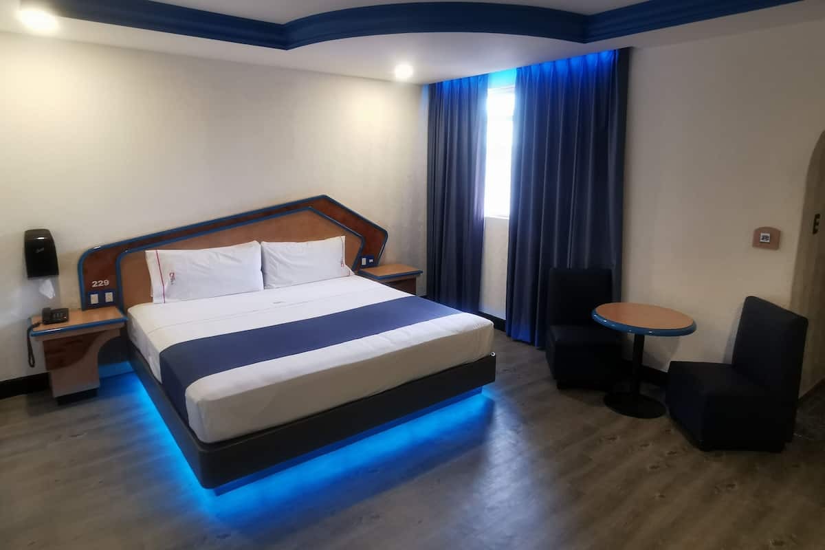 Une chambre d’hôtel avec un lit, des tables de chevet, une petite table avec des chaises et une fenêtre avec des rideaux.