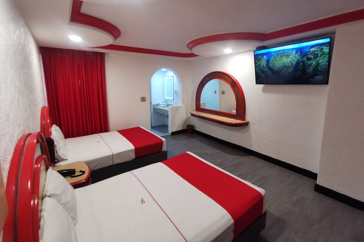 Une chambre d’hôtel avec deux lits, une télévision, un miroir et une salle de bain visible à travers une arche.