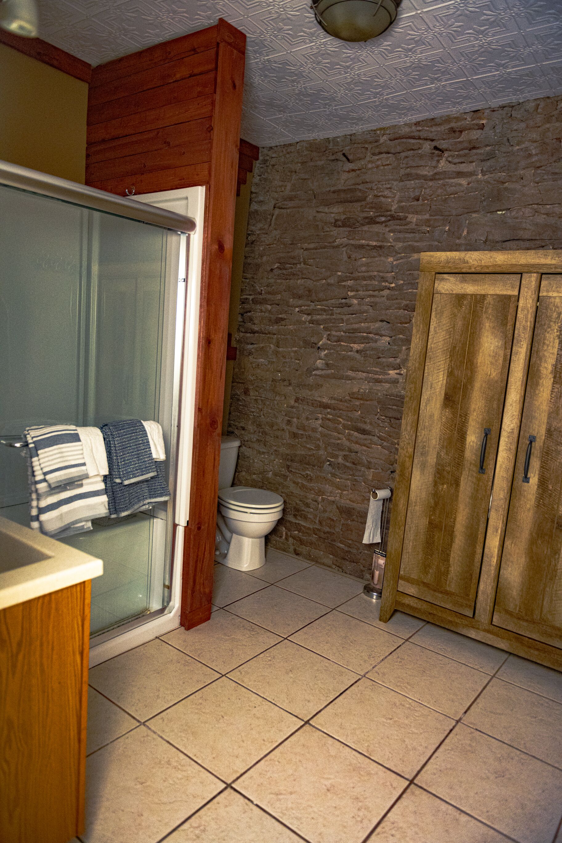 A bathroom with a wooden cabinet, a toilet, and a glass shower enclosure.