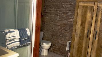 A bathroom with a wooden cabinet, a toilet, and a glass shower enclosure.