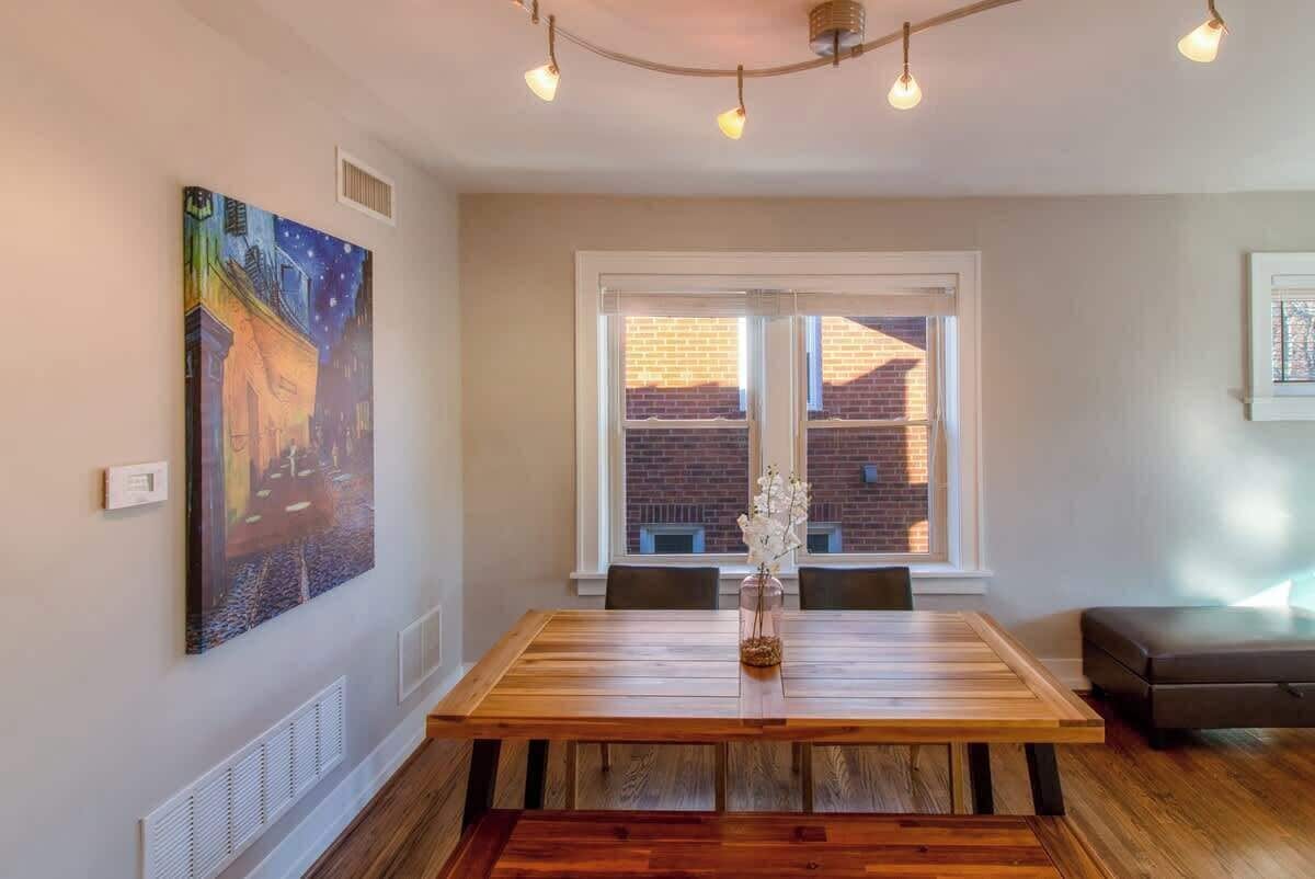 Un comedor con una mesa de madera, sillas, un cuadro en la pared, un ventanal con vistas y una lámpara en el techo.
