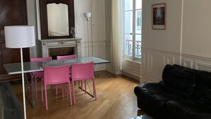 Ein Wohnzimmer mit einem Glastisch, einer schwarzen Ledersofa, einem Esstisch mit rosa Stühlen, einer Lampe und einem Kamin.