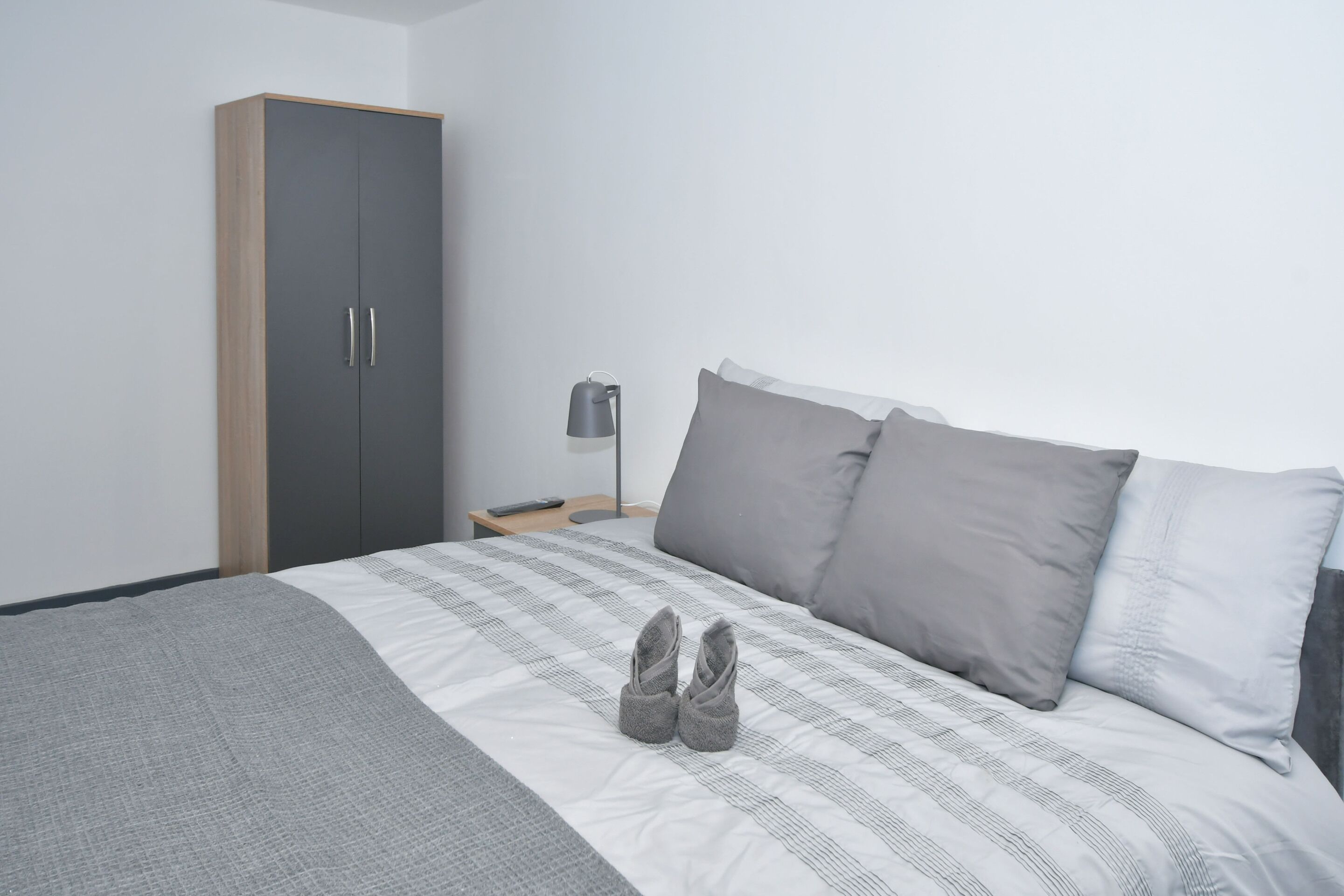 Une chambre à coucher avec un lit, des oreillers gris, une couverture grise, une armoire et une lampe de chevet.