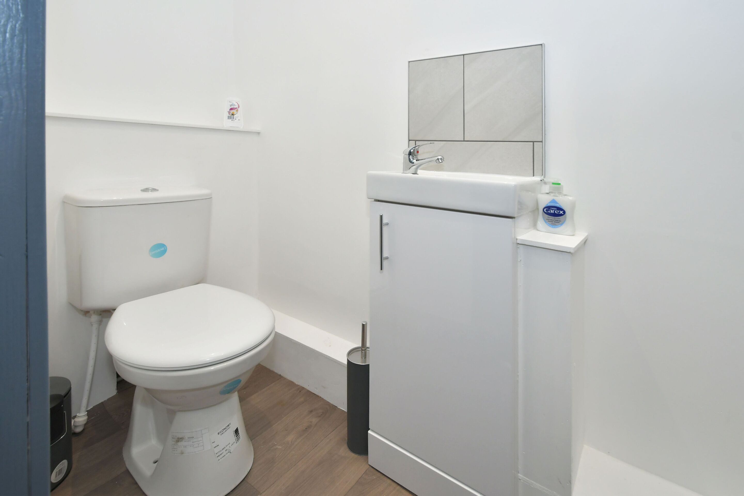 Un baño pequeño con inodoro blanco, lavamanos y un mueble auxiliar.