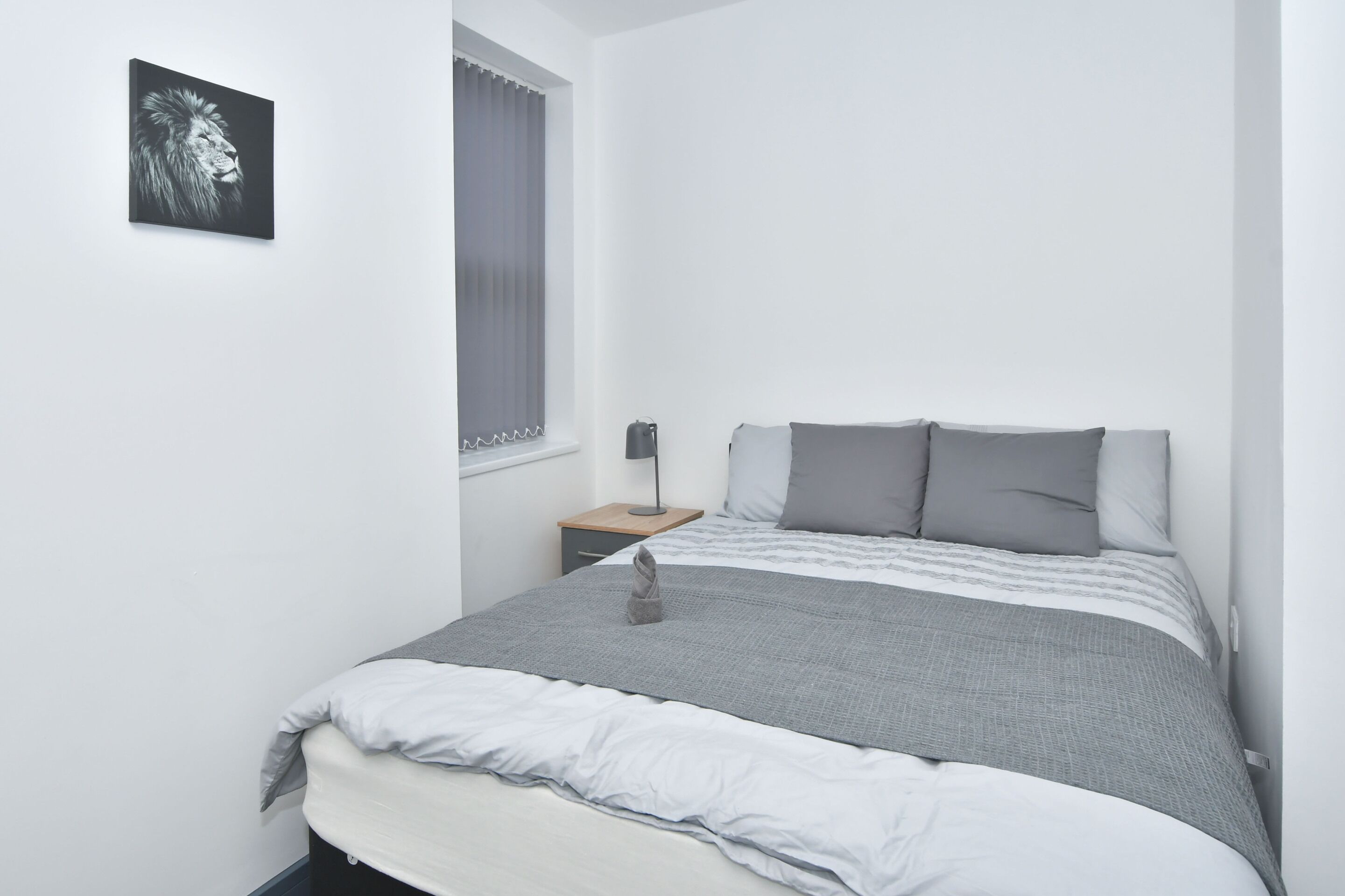 A bedroom with a bed, pillows, a bedside table, a lamp, and a window with curtains.