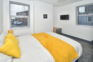 Una habitación de hotel con cama, televisor, mesita de noche y ventana con persianas.