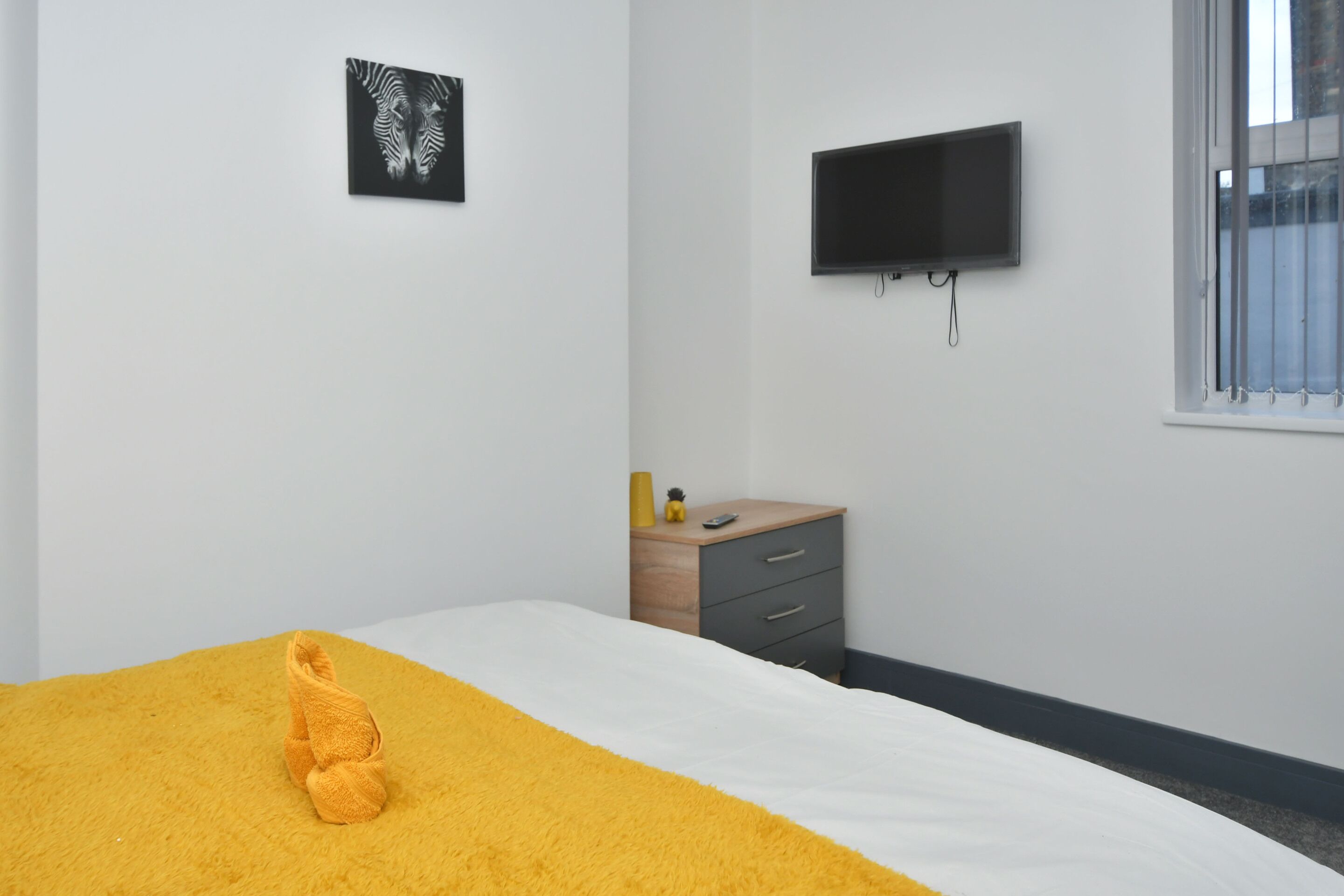 Un dormitorio con cama, televisión, mesita de noche de madera y ventana.