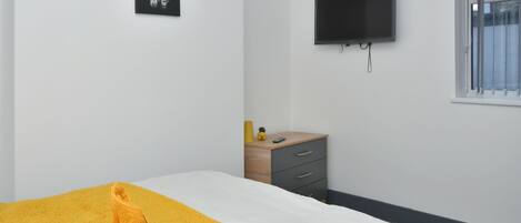 Un dormitorio con cama, televisión, mesita de noche de madera y ventana.