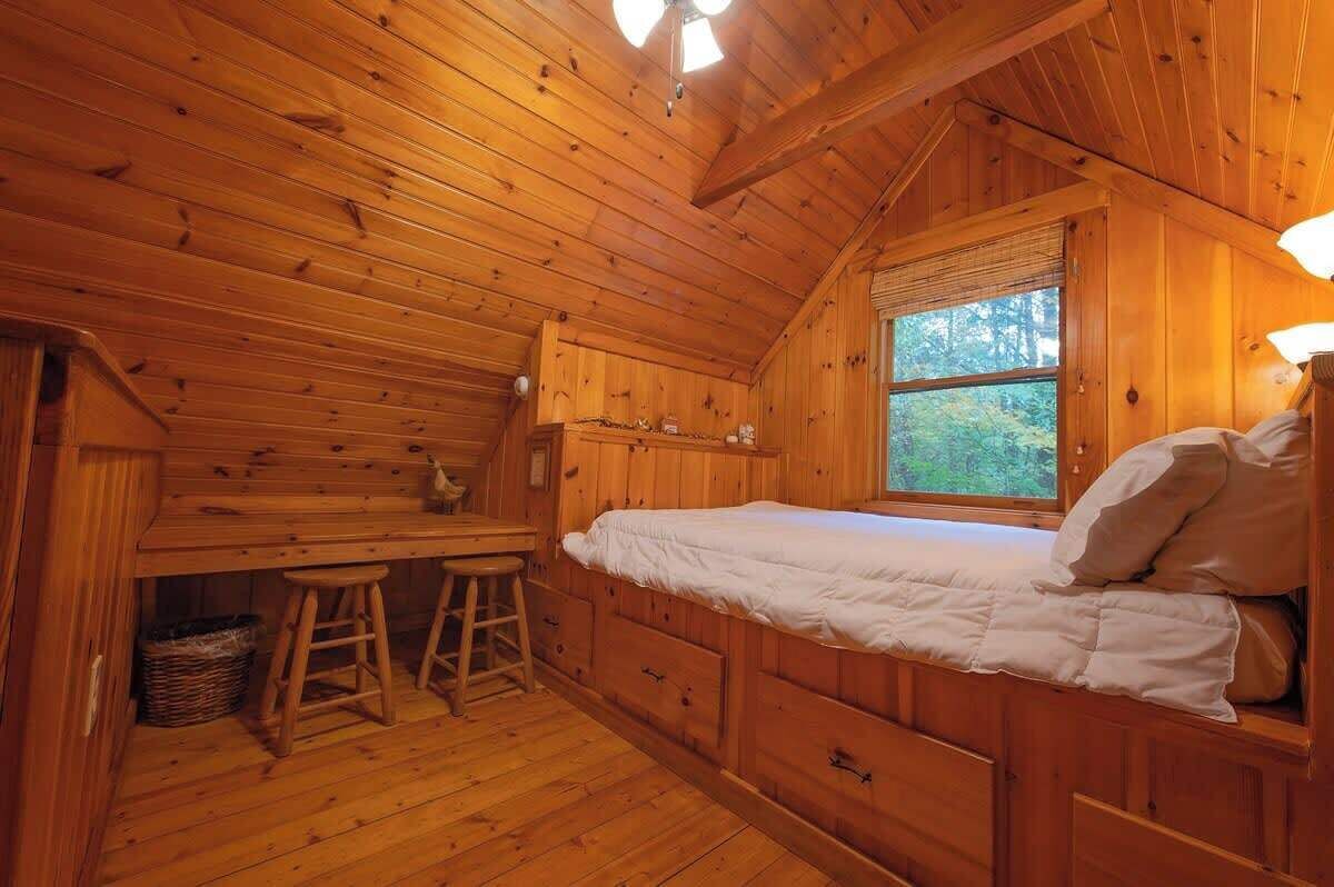 Interior de una cabaña de madera con una cama, un escritorio y una ventana.