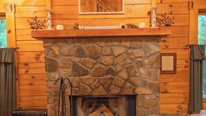 A stone fireplace with a wooden mantel, a mirror above it, and a log storage area. - Cherokee private cabin in Riverside Resort (Benton)