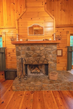 A stone fireplace with a wooden mantel, a mirror above it, and a log storage area. - Cherokee private cabin in Riverside Resort (Benton)
