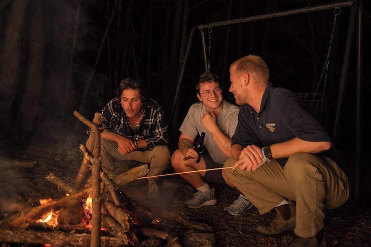 Three people sitting by a campfire at night.