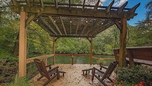 A wooden deck with chairs and a pergola overlooking a pond. - Cherokee private cabin in Riverside Resort (Benton)