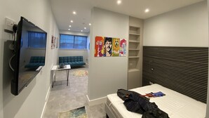 A modern bedroom with a bed, a sofa, a small table, and a wall with artwork. - Kempston Suites Liverpool Apartment 3 (Liverpool)