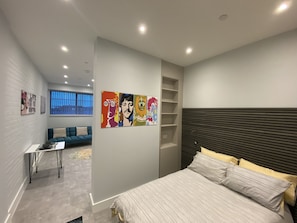 A modern bedroom with a bed, a sofa, a small table, and a wall with colorful artwork.