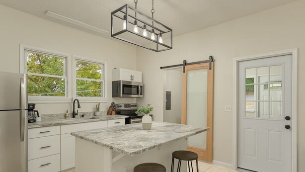 A modern kitchen with white cabinetry, a central island with stools, a sliding glass door, and a hanging light fixture.