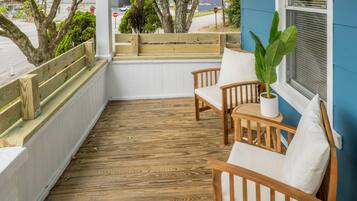 A wooden deck with a bench and two chairs, a potted plant, and a window with blinds.