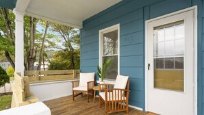 A porch with a wooden table and chairs, a white door with a window, and a doormat with text.