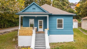 A two-story house with a front porch, a wooden deck, and a staircase leading to the entrance.