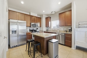 A modern kitchen with wooden cabinets, stainless steel appliances, and a granite countertop island. - The Red Arroyo House (Alamogordo)
