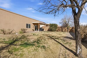 A single-story house with a covered patio, a small front yard with sparse grass, and a tree in the foreground.