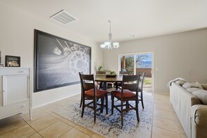 A dining area with a table and chairs, a chandelier, and a large painting on the wall. - The Red Arroyo House (Alamogordo)