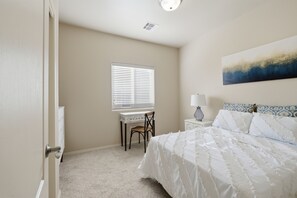 A bedroom with a bed, a desk, a chair, and a window with blinds. - The Red Arroyo House (Alamogordo)