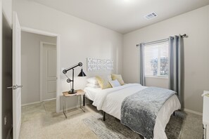 A bedroom with a bed, a nightstand, a lamp, a window with curtains, and a door.