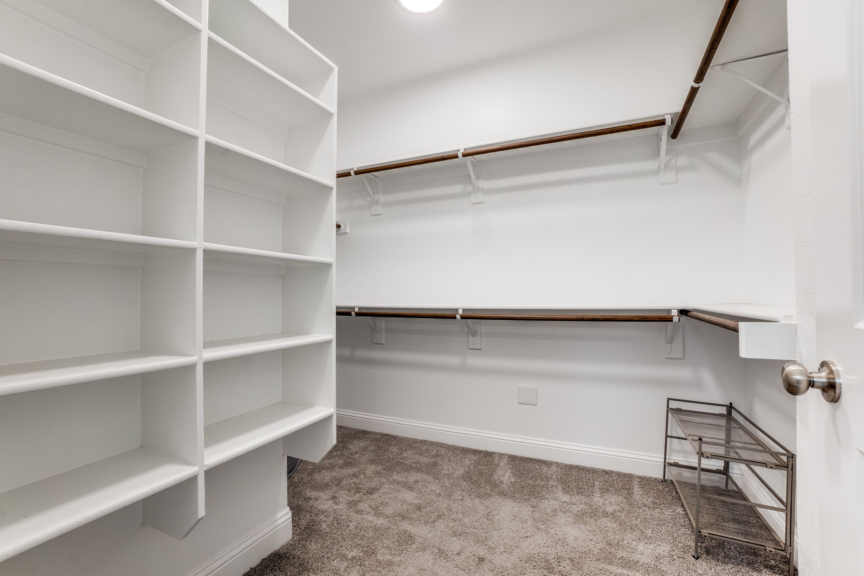 A walk-in closet with open shelving, a metal rack, and a door with a silver handle.