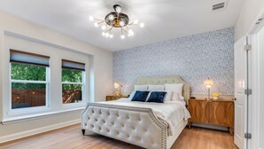 A bedroom with a tufted headboard bed, two bedside lamps, a wooden nightstand, and a patterned wallpaper.