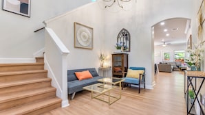 A spacious living area with a staircase, a blue sofa, a glass coffee table, and a chandelier.