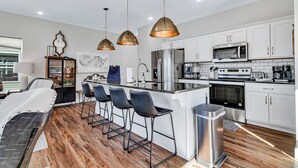 Una cocina moderna con armarios blancos, electrodomésticos de acero inoxidable y una barra con taburetes.
