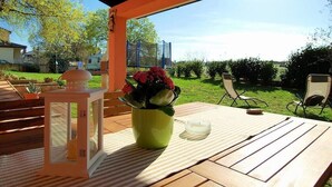 Une terrasse extérieure avec une table en bois, une plante en pot, une lanterne et des chaises d’extérieur.
