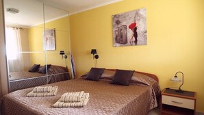 Une chambre à coucher avec un grand lit, deux tables de chevet, un miroir et une lampe fixée au mur.
